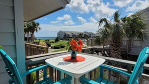 Ein Balkon mit türkisfarbenen Stühlen, einem weißen Tisch und einer Vase mit roten Blumen.
