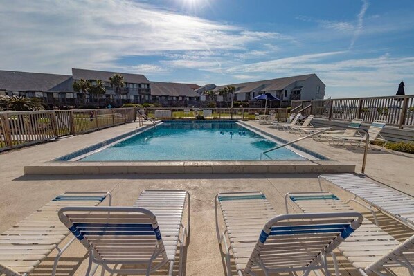 A rectangular swimming pool with lounge chairs and a wooden fence surrounding it. - Gulf views, community pool, 60 seconds to the beach! (St. George Island)
