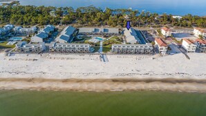 Eine Luftaufnahme eines Küstenhotels mit mehreren Gebäuden, einem Strand und einem Schwimmbad.