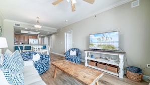 A living room with a wooden coffee table, blue patterned sofa, and a television on a white stand. - Seawind 1402 | Updated condo with perfect beach view and walk to dine, shop, more! (Gulf Shores)