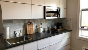 Une cuisine moderne avec des meubles blancs, un plan de travail noir et un évier en acier inoxydable.