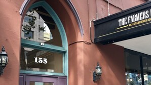 Un immeuble avec une porte violette portant l’inscription « San Pedro Square Apartments » et un auvent noir sur lequel on peut lire « The Farmers ».