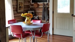 Un interior de madera con una mesa de comedor, sillas rojas, una araña y una ventana con vistas.