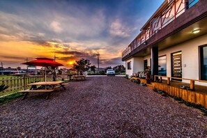 A gravel driveway leading to a building with a covered outdoor seating area and a car parked in front.