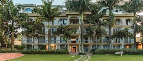 A multi-story hotel with a central courtyard, surrounded by palm trees and a pathway leading to the entrance.