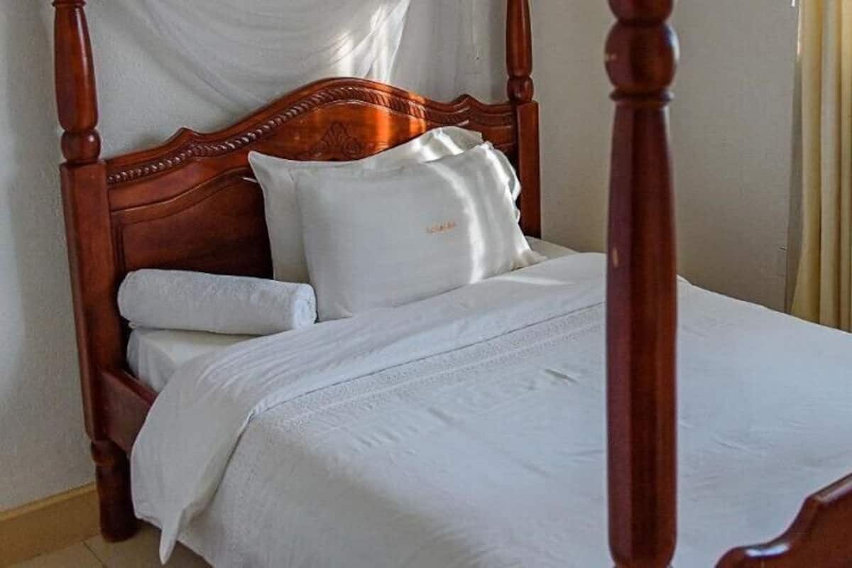 A four-poster bed with white linens and a wooden headboard.