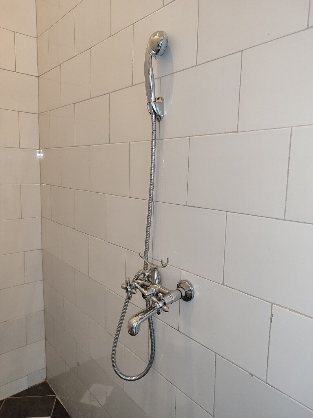 A shower with a handheld showerhead and a fixed wall-mounted faucet.