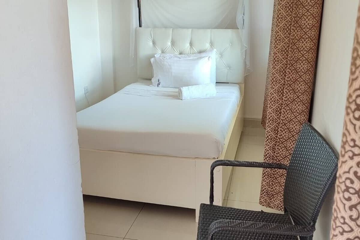 A small, neatly arranged bedroom with a single bed, a chair, and a patterned curtain.
