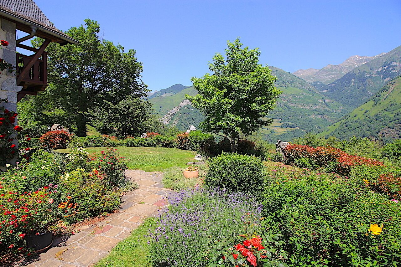 A garden with a stone pathway, lush greenery, and a mountain backdrop.