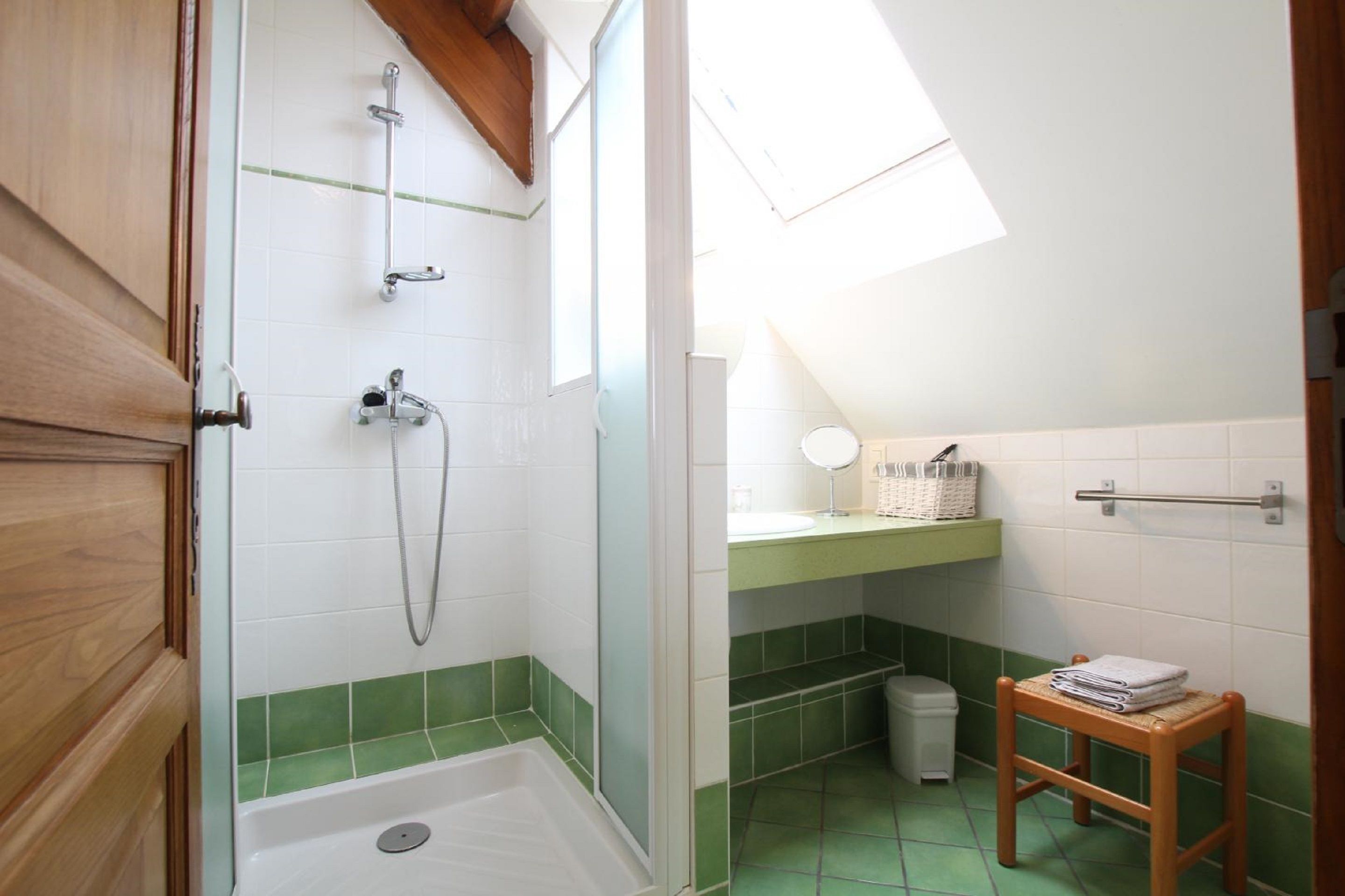 Un baño con ducha, lavabo, espejo y un taburete de madera pequeño.