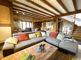 Una sala de estar acogedora con un sofá seccional, vigas de madera, un comedor y una escalera.