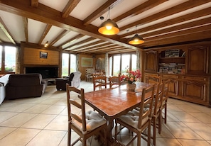 Amplia sala de estar con una mesa de comedor de madera, sillas acolchadas, una chimenea y una cocina con armarios de madera.