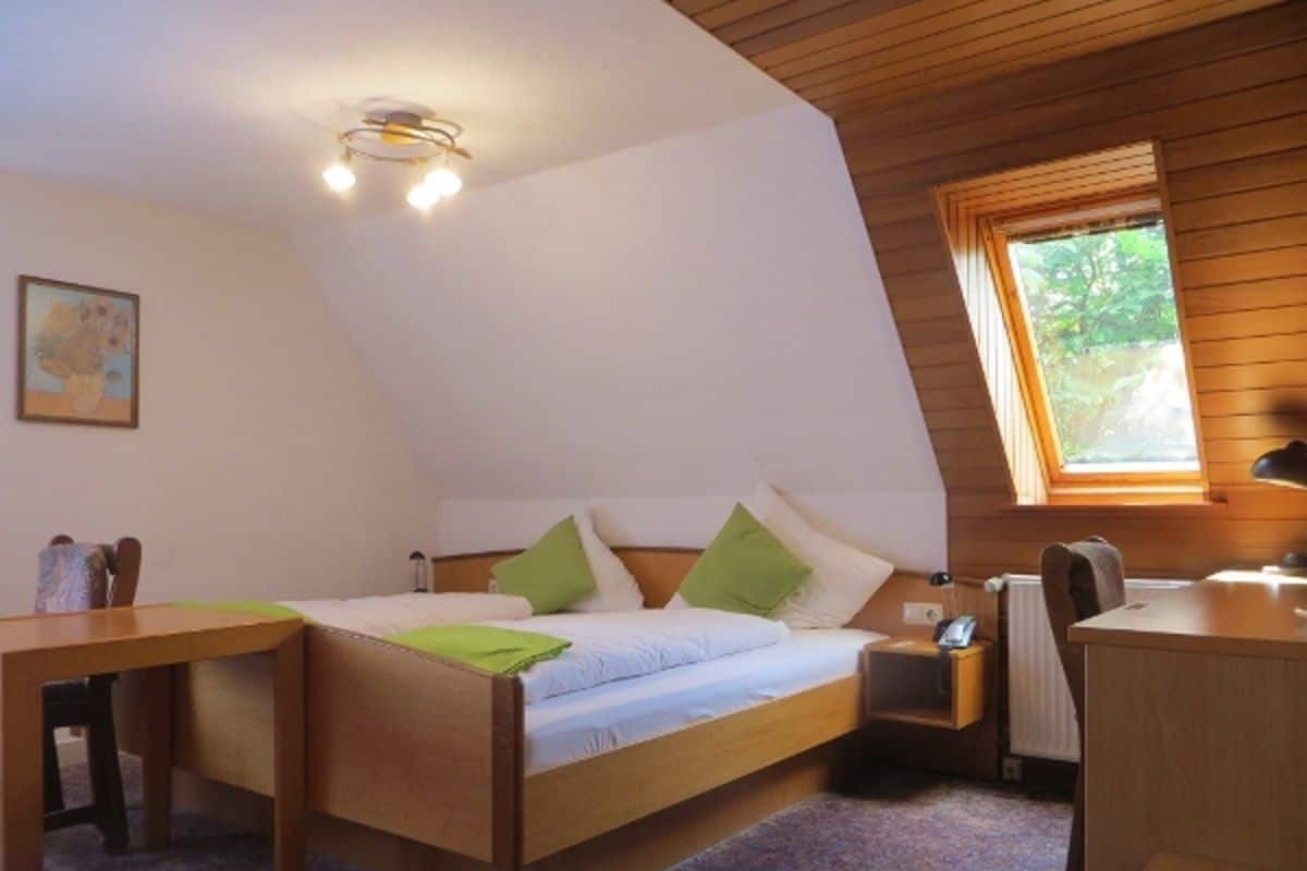 A bedroom with a bed, bedside table, desk, and a window.