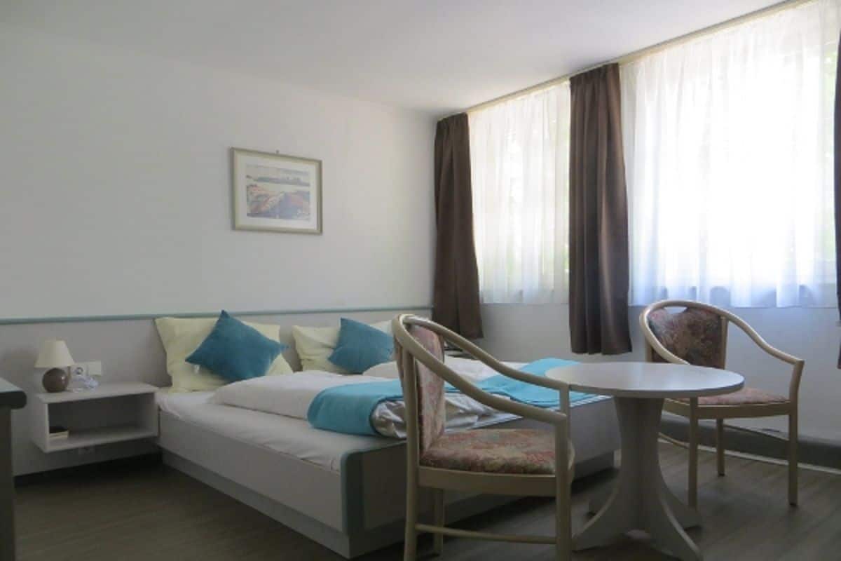 A hotel room with a bed, two chairs, a small table, a nightstand, and a window with curtains.