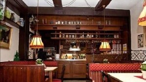Um restaurante acolhedor com assentos e mesas de madeira, um bar com prateleiras de garrafas e luminárias pendentes.