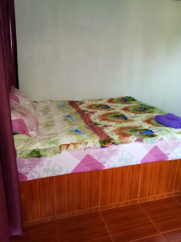 A bedroom with a bed covered in a colorful quilt, a purple pillow, and a wooden headboard. - Rai Rames Agritourism (Khao Kho)