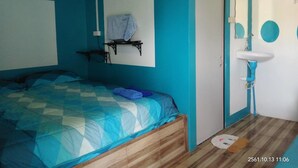 A bedroom with a bed, a wall-mounted shelf, a door, and a sink.