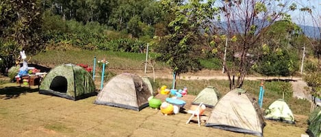 Un campamento con varias tiendas de campaña y sillas de camping dispuestas en un campo cubierto de hierba.
