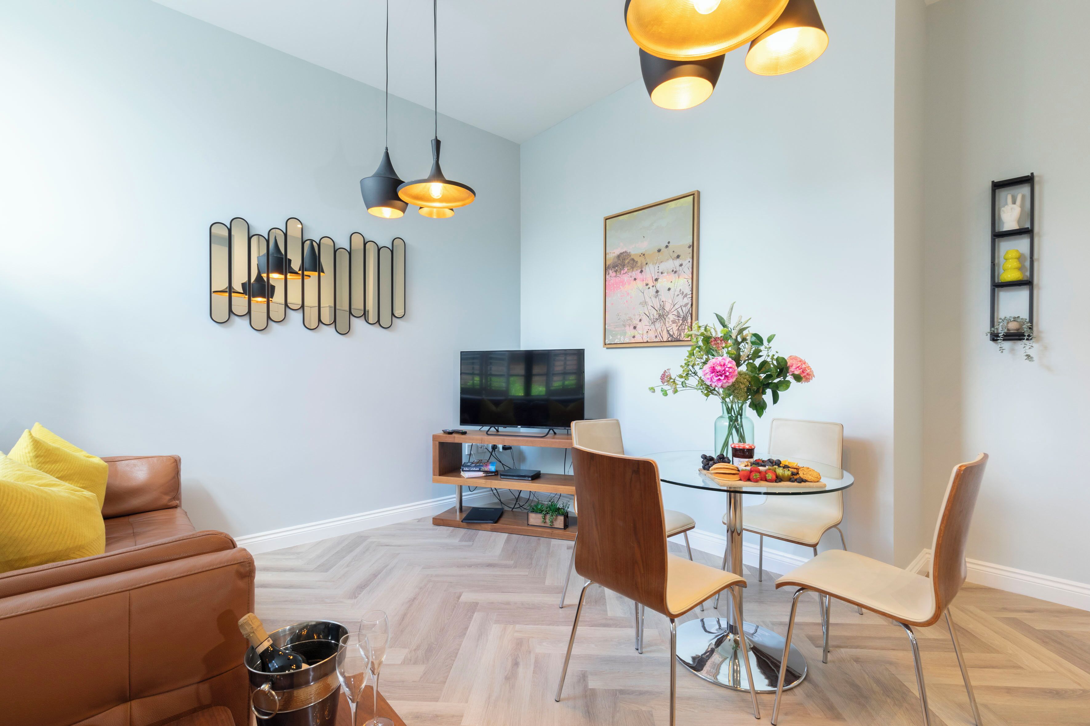Un salon moderne avec un canapé en cuir marron, une table à manger en verre avec des chaises, un téléviseur posé sur un meuble en bois et un élément décoratif mural.