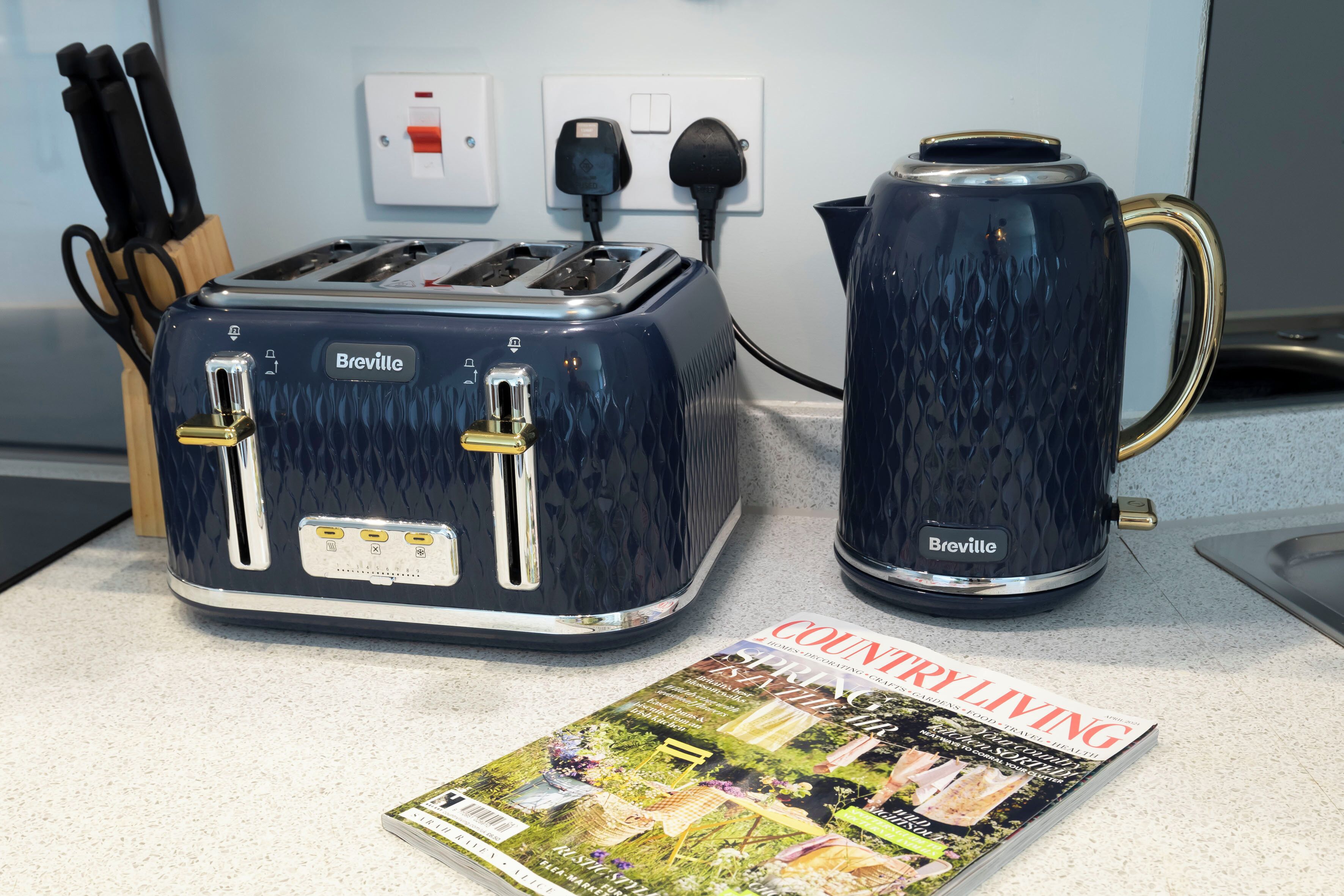 Un grille-pain et une bouilloire de la marque Breville sont posés sur un plan de travail de cuisine, à côté d’un magazine intitulé « COUNTRY LIVING ».