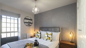 Una cama bien hecha con una bandeja de desayuno, una lámpara de noche y una pared con un estampado geométrico.