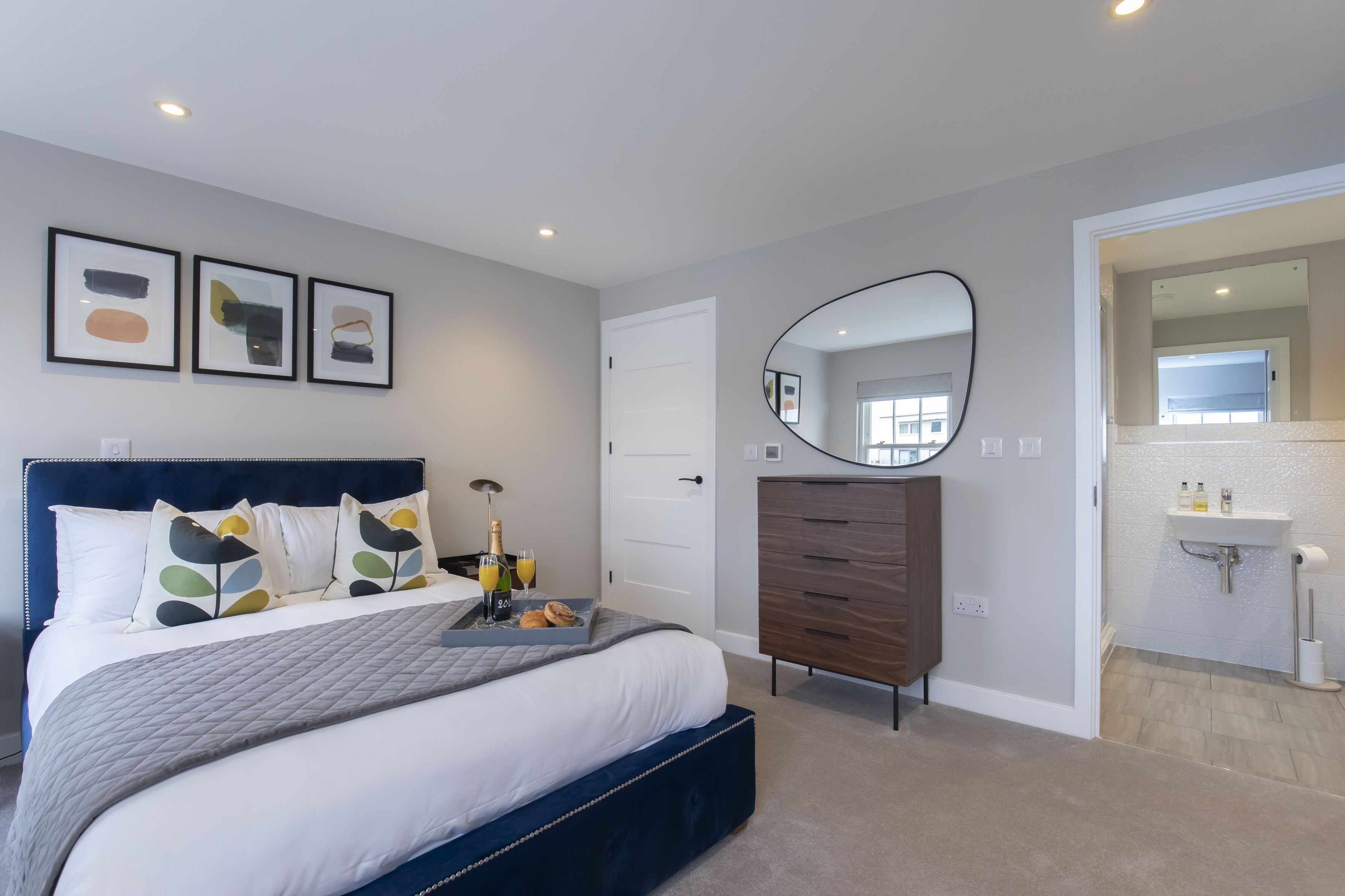 Un dormitorio moderno con una cama grande, un tocador, un espejo y obras de arte en la pared.