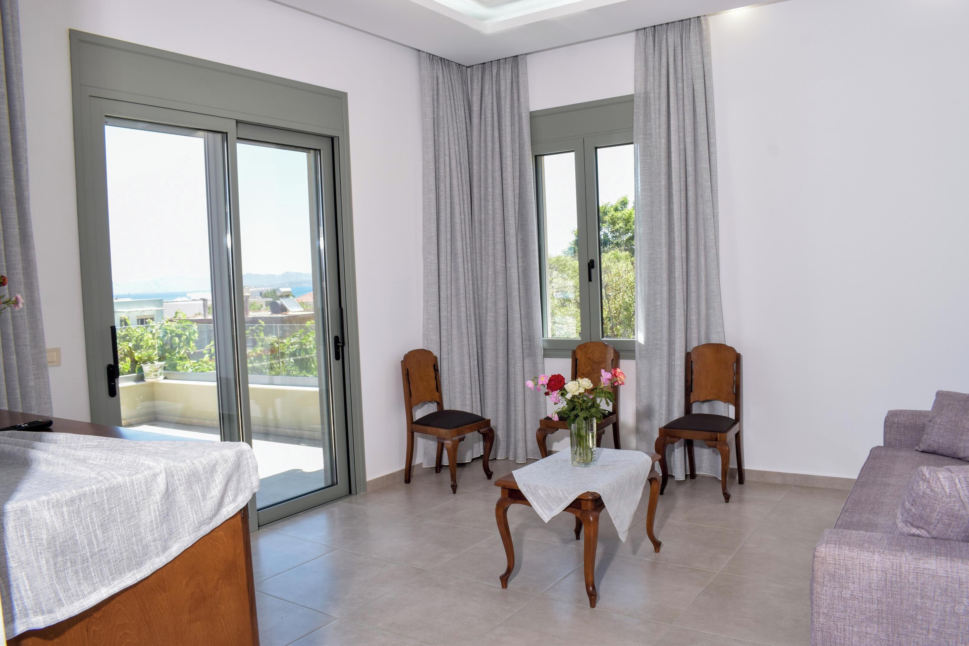 A room with a balcony, two wooden chairs, a table with a vase of flowers, and a sofa.