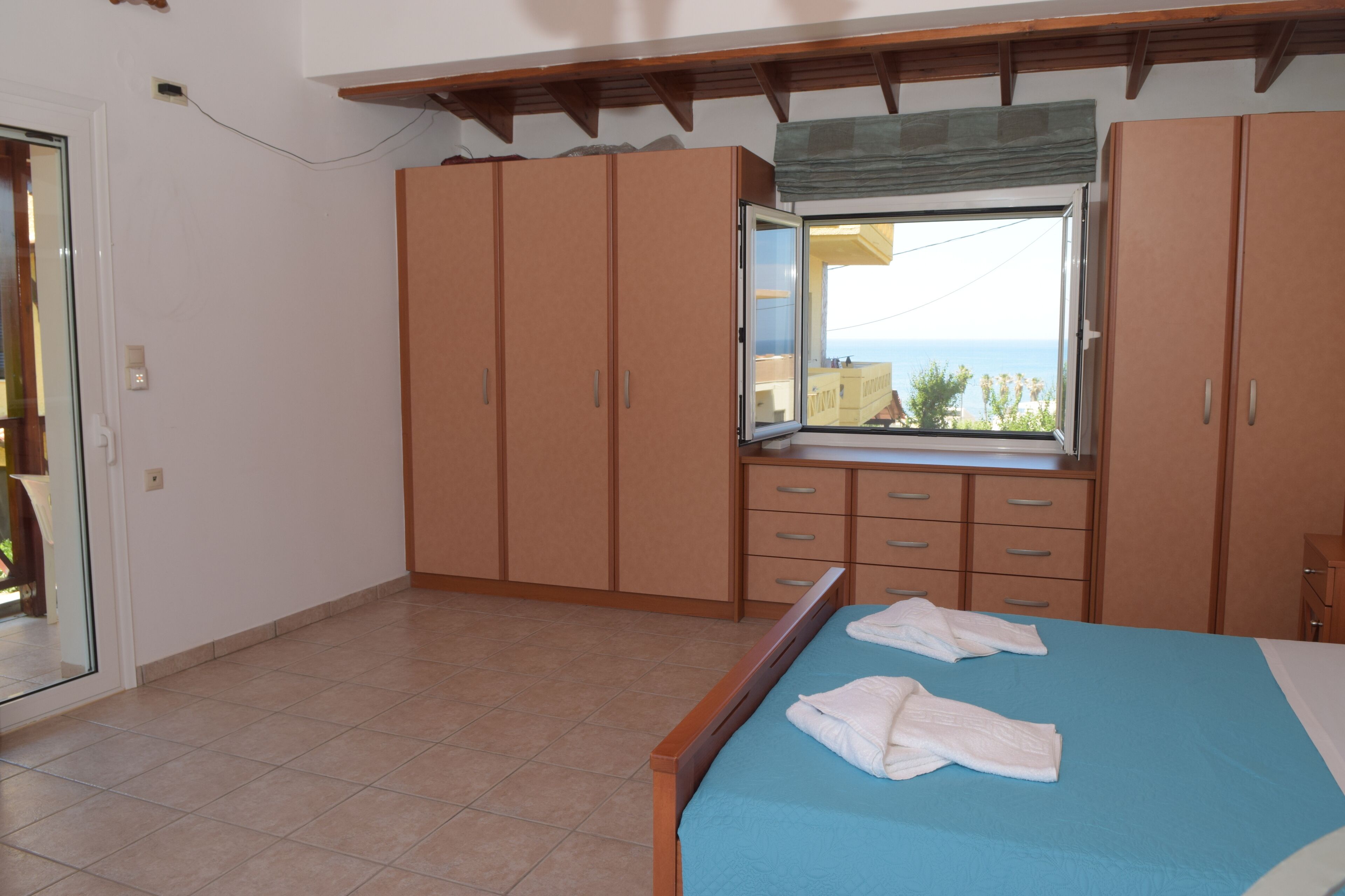 A bedroom with a bed, a window with a view, and wooden wardrobes.
