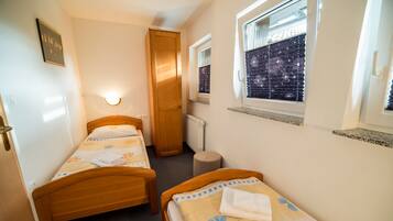 A small, clean room with two single beds, a wooden wardrobe, a radiator, and a window with a starry view.
