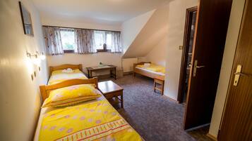 Een slaapkamer met twee eenpersoonsbedden, een klein tafeltje en een raam met gordijnen.