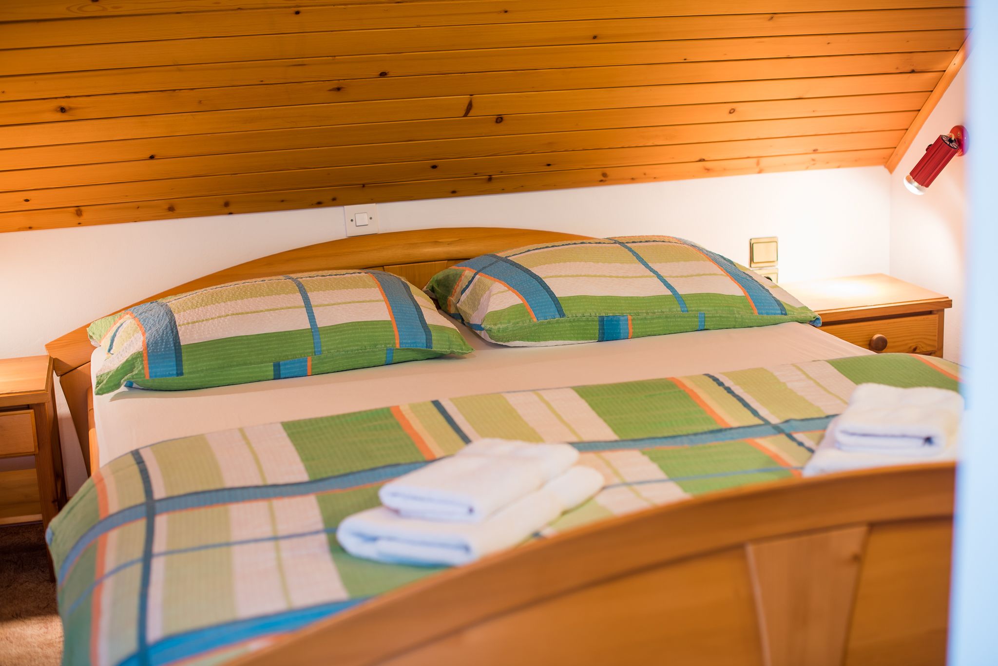 Una cama bien hecha con ropa de cama a rayas y dos almohadas, un cabecero de madera y una mesita de noche con una lámpara.