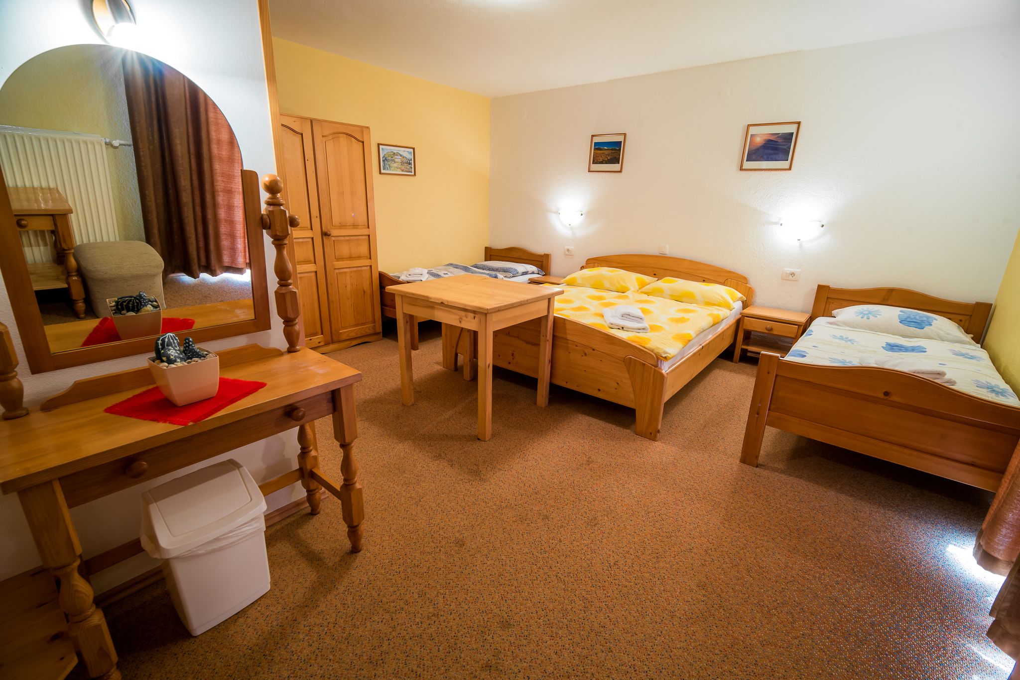 A room with two single beds, a wooden desk with a chair, a mirror, and a small trash bin.