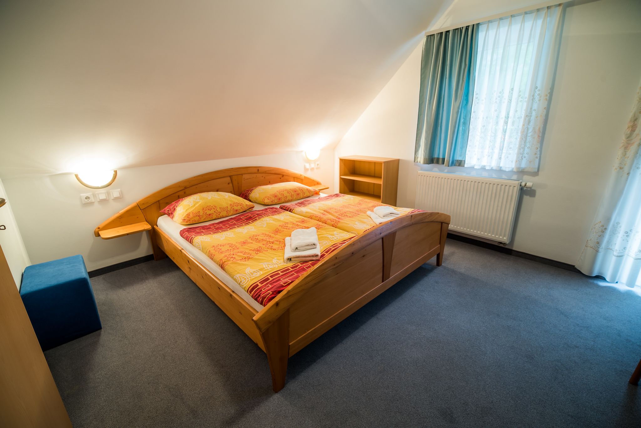 A bedroom with a wooden bed, two bedside tables, a radiator, and a window with curtains.