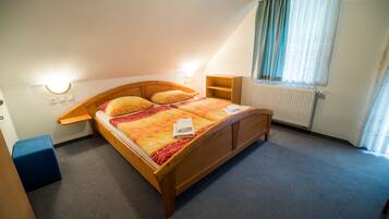 A bedroom with a wooden bed, two bedside tables, a radiator, and a window with curtains.