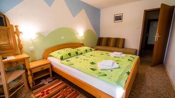 A bedroom with a bed, a desk, a chair, a nightstand, a lamp, and a door.