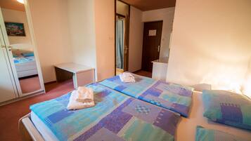 Un dormitorio con dos camas, una mesita de noche, un espejo y una puerta que da a otra habitación.