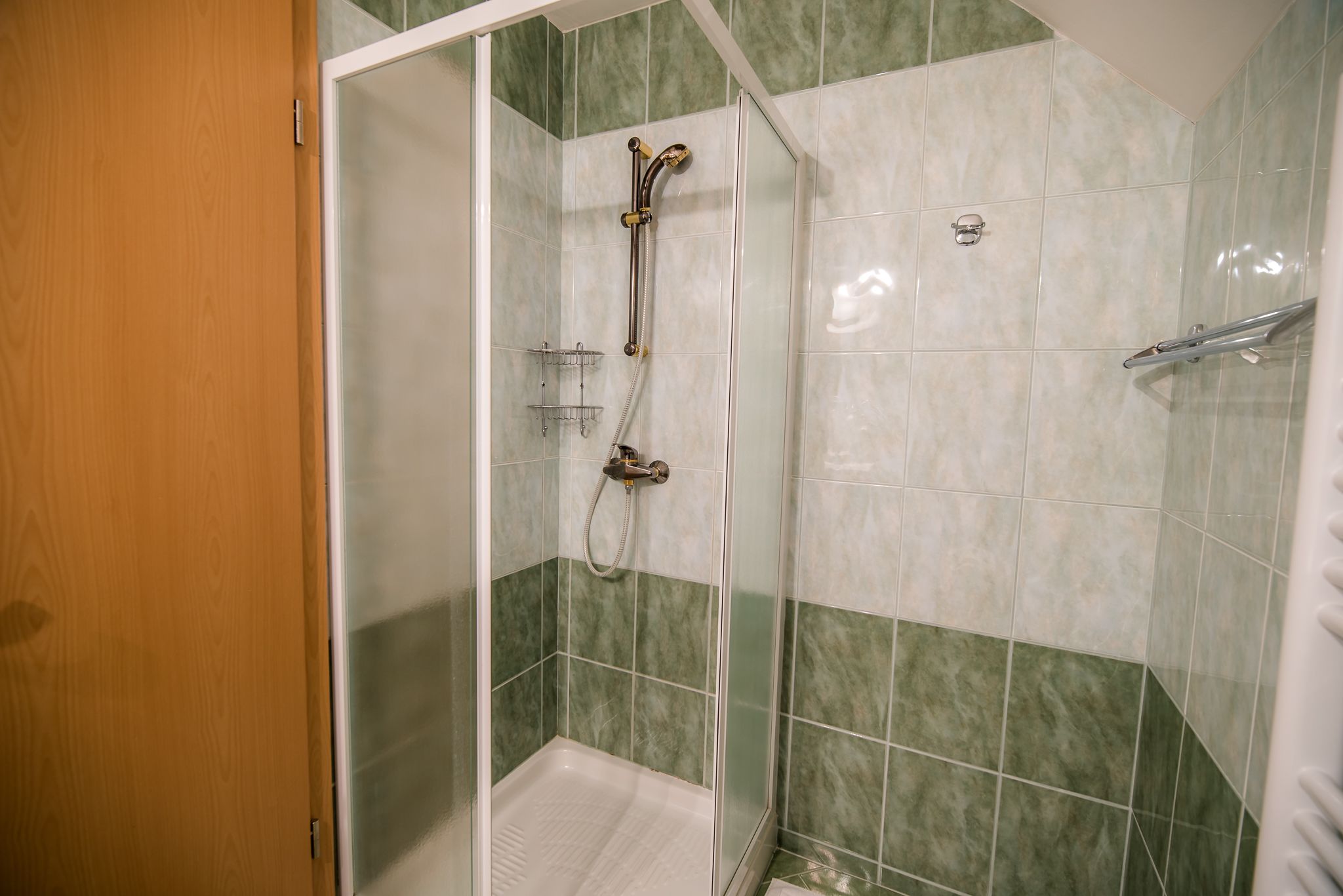 Doccia con porta in vetro, soffione metallico e doccetta a mano.