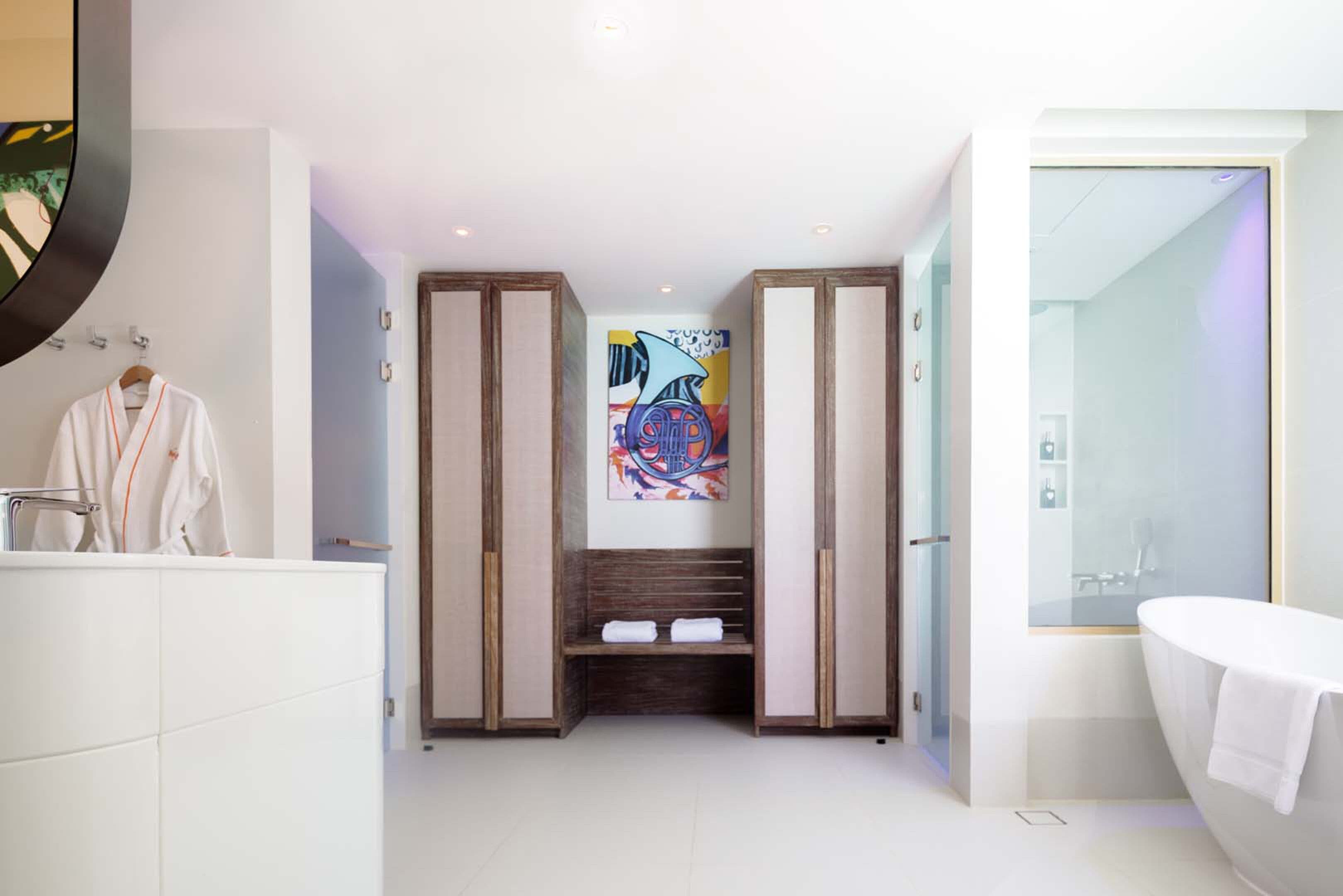 A modern bathroom with a large mirror, a white bathtub, and a bench with towels.