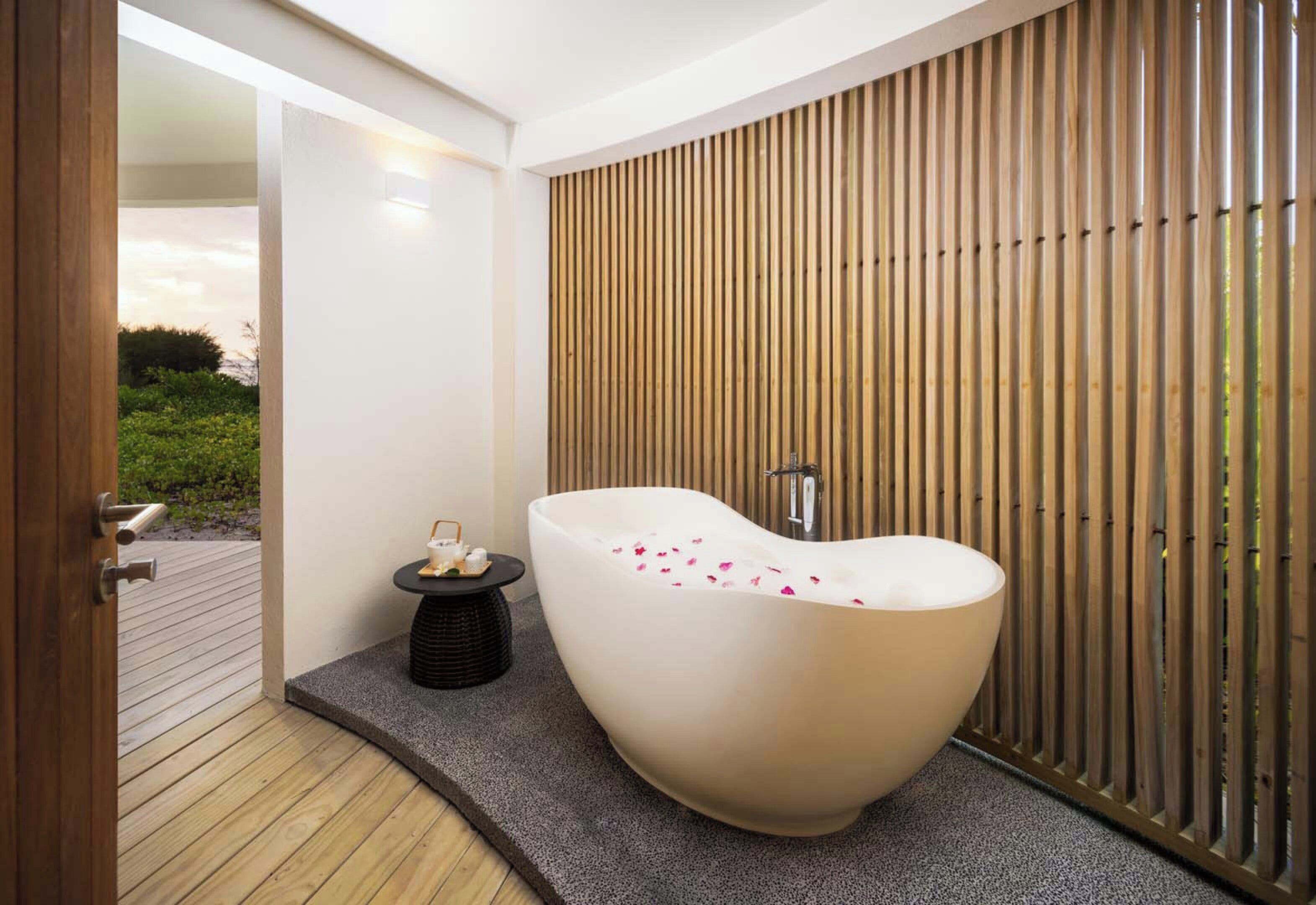 Un baño moderno con una bañera independiente, una mesita con artículos de aseo y una pared de listones de madera.