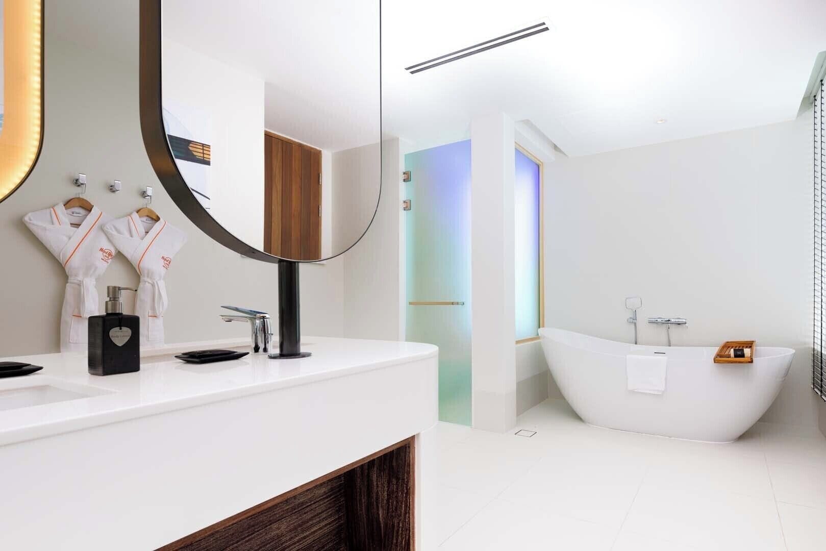 A modern bathroom with a white vanity, a freestanding bathtub, and a large mirror.