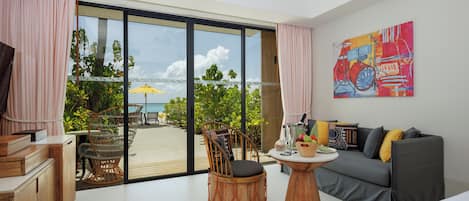 A room with a view of the beach, a sofa, a wooden table, and a chair.