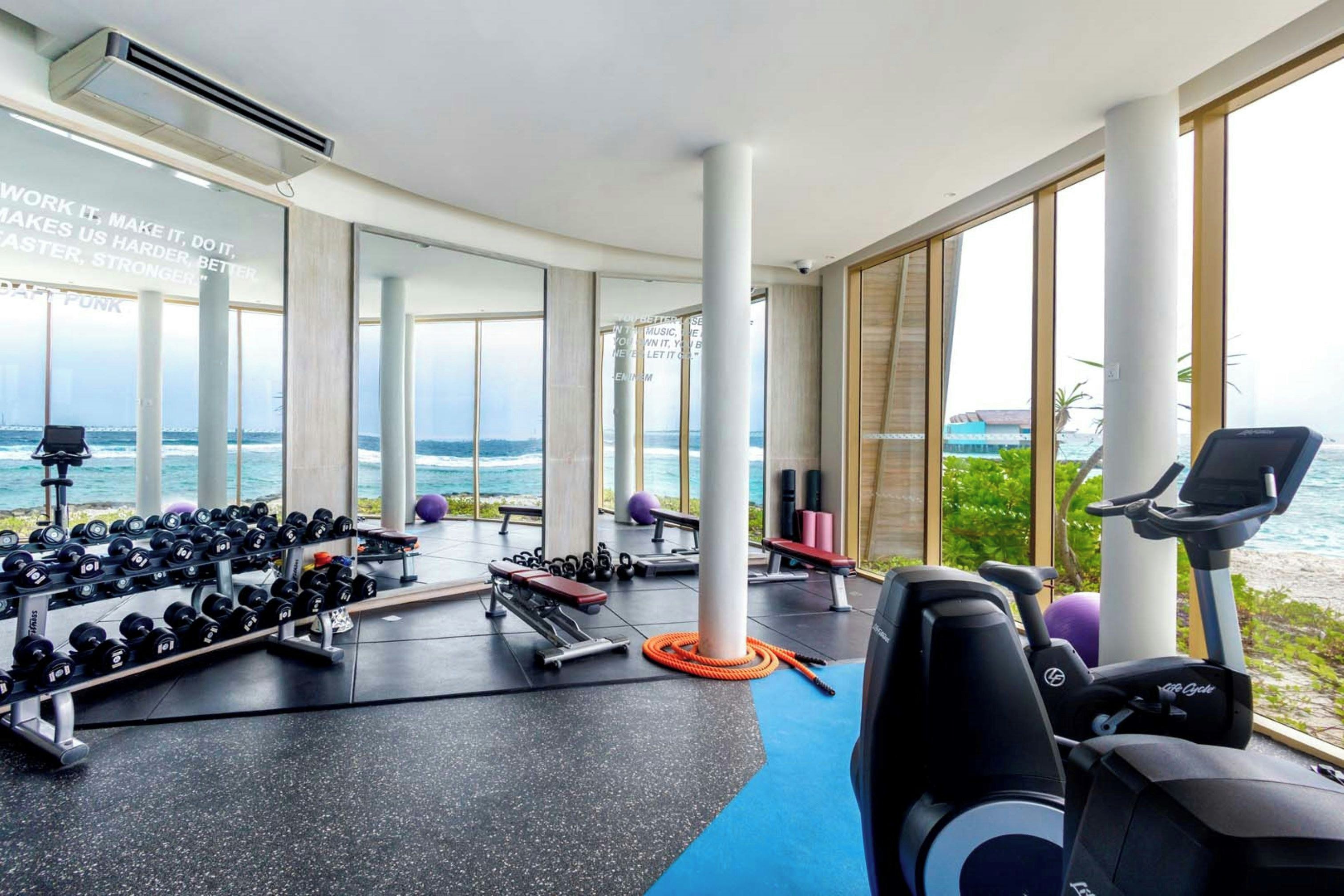 Een sportschool met uitzicht op de oceaan, voorzien van fitnessapparatuur, gewichten en cardioapparaten.