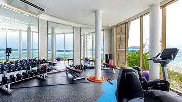 Een sportschool met uitzicht op de oceaan, voorzien van fitnessapparatuur, gewichten en cardioapparaten.