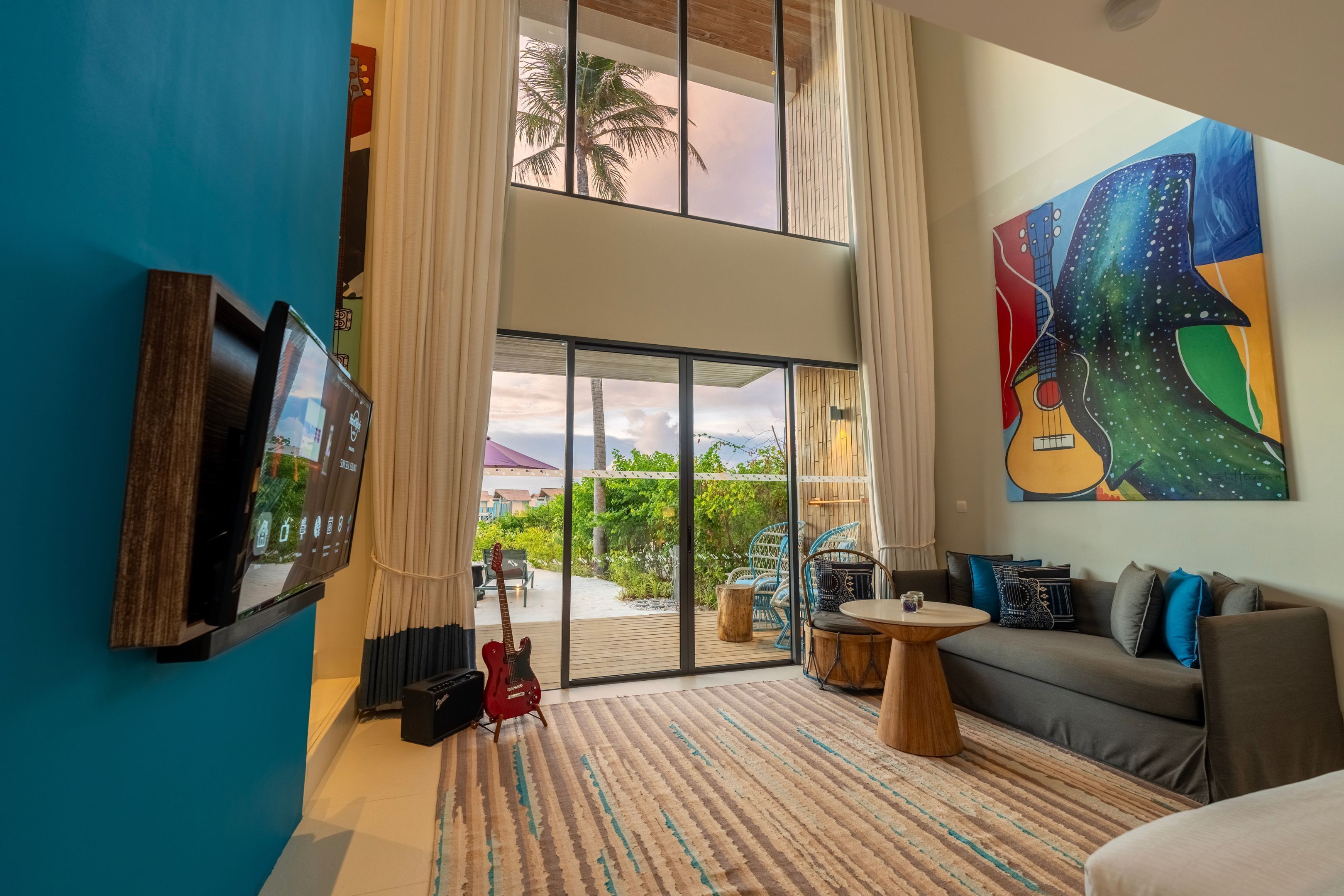 A modern living room with a large TV, a guitar, a sofa, and a colorful painting.
