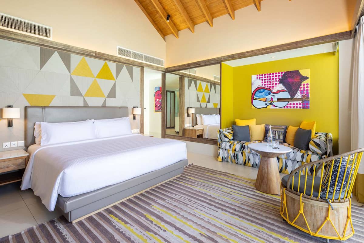 Une chambre d’hôtel moderne avec un grand lit, un ensemble de canapés, une petite table ronde et une chaise.