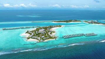 Vue aérienne d’un complexe hôtelier tropical doté de bungalows sur pilotis, d’un ensemble de bâtiments principaux et d’une plage.