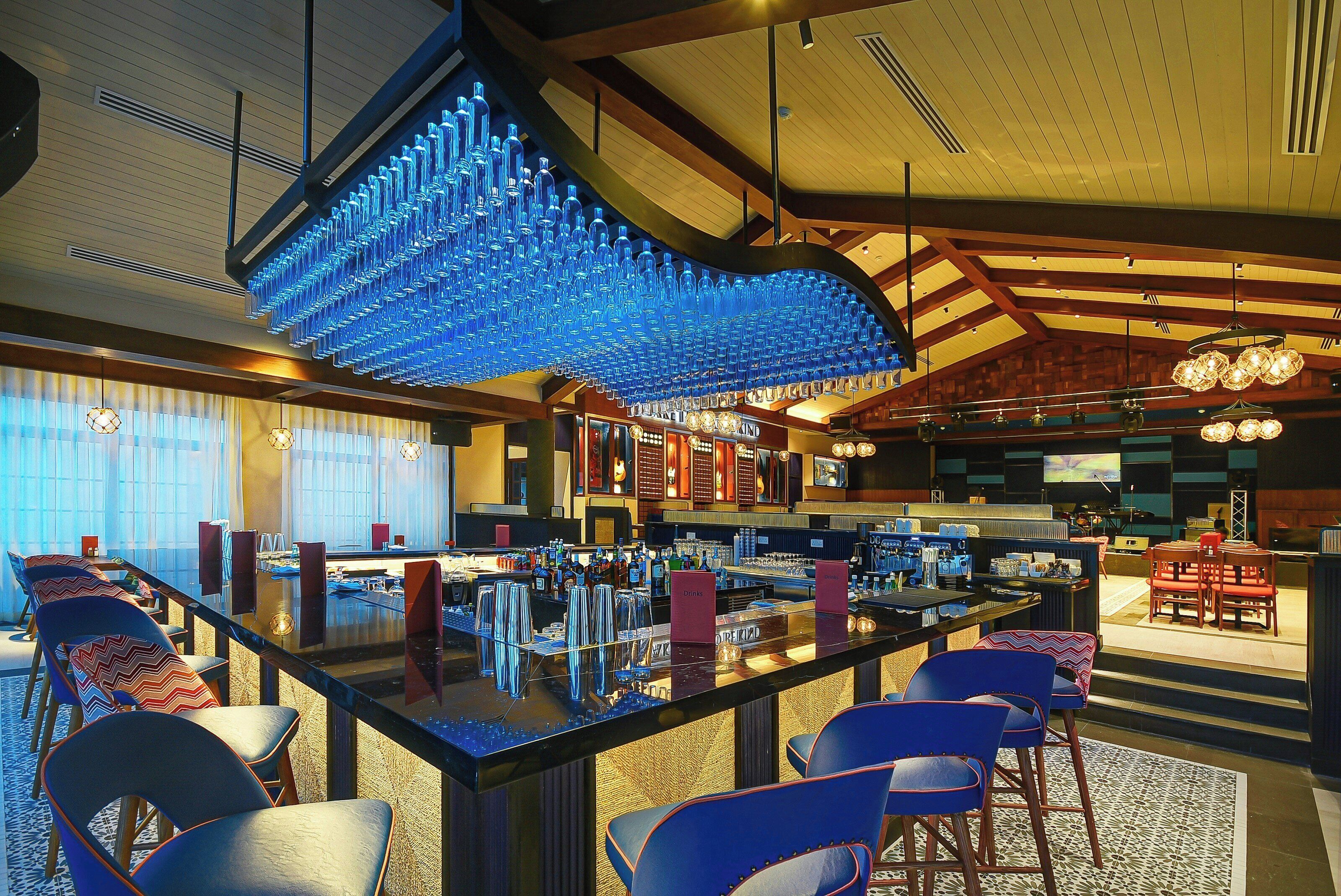 A bar area with a long counter, bar stools, and a ceiling with hanging blue glass-like decorations.