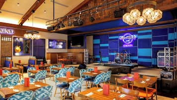 A restaurant with a stage, tables, chairs, and a neon sign.