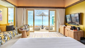 Habitación de hotel con cama, televisión, escritorio de madera, una mesa con una bebida y vista al mar.