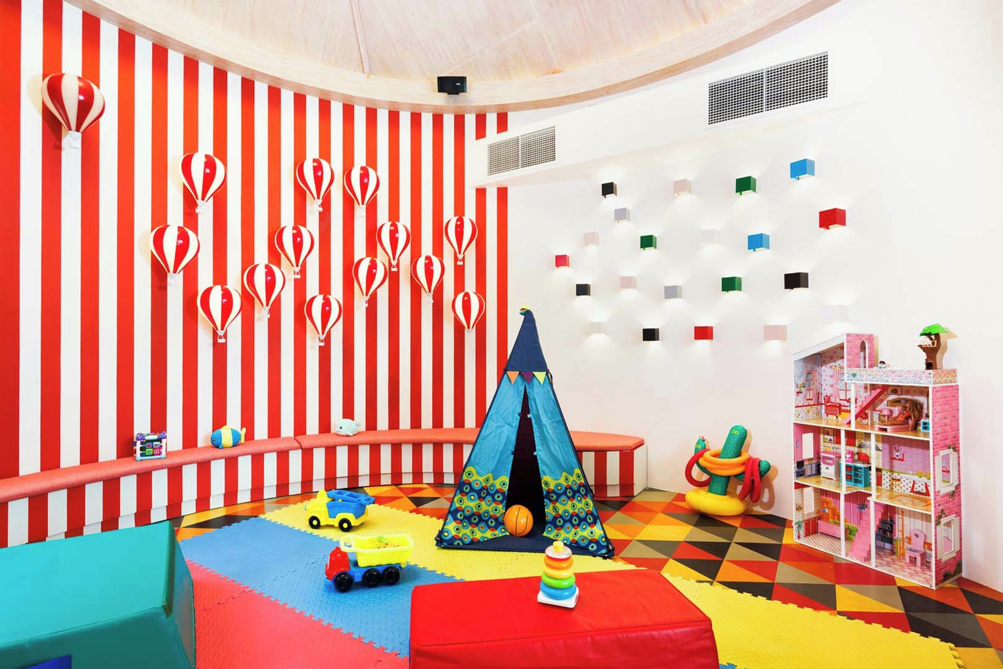 Una sala de juegos con pared a rayas, una tienda de campaña y una casa de muñecas.